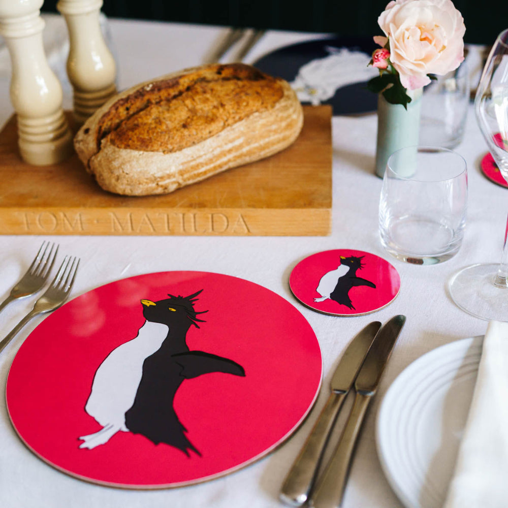 Table setting with a red plate featuring a penguin design, bread, and cutlery.