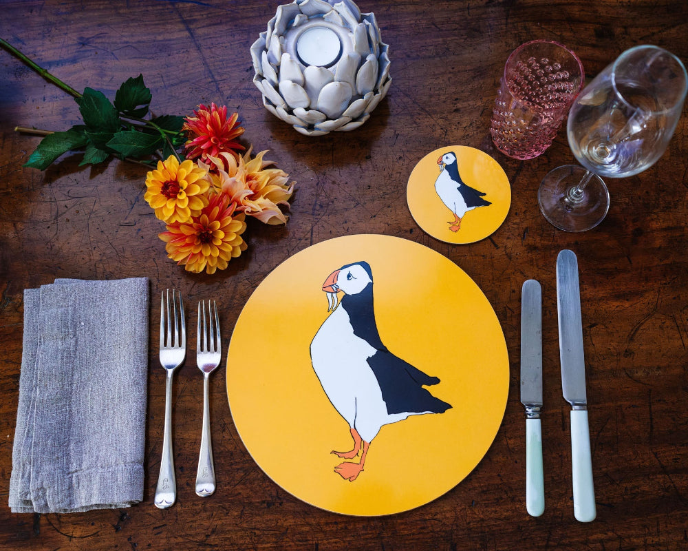 Table setting with a puffin-themed placemat on a wooden table.
