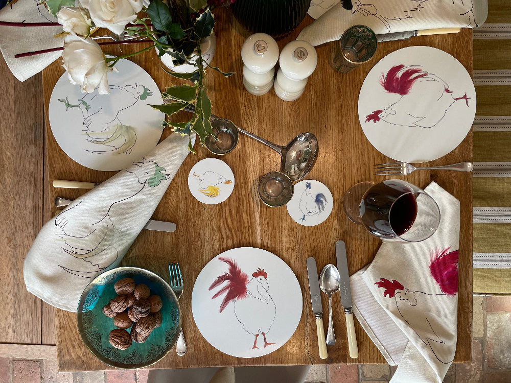 Dining table setting with rooster-themed plates, napkins, and cutlery on a wooden table.