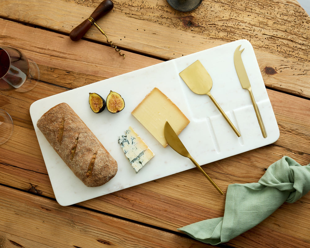Cheeseboard with bread, figs, and gold cheese knives on a wooden table.