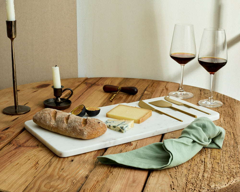 Wooden table with bread, cheese, wine glasses, and candles on a neutral background