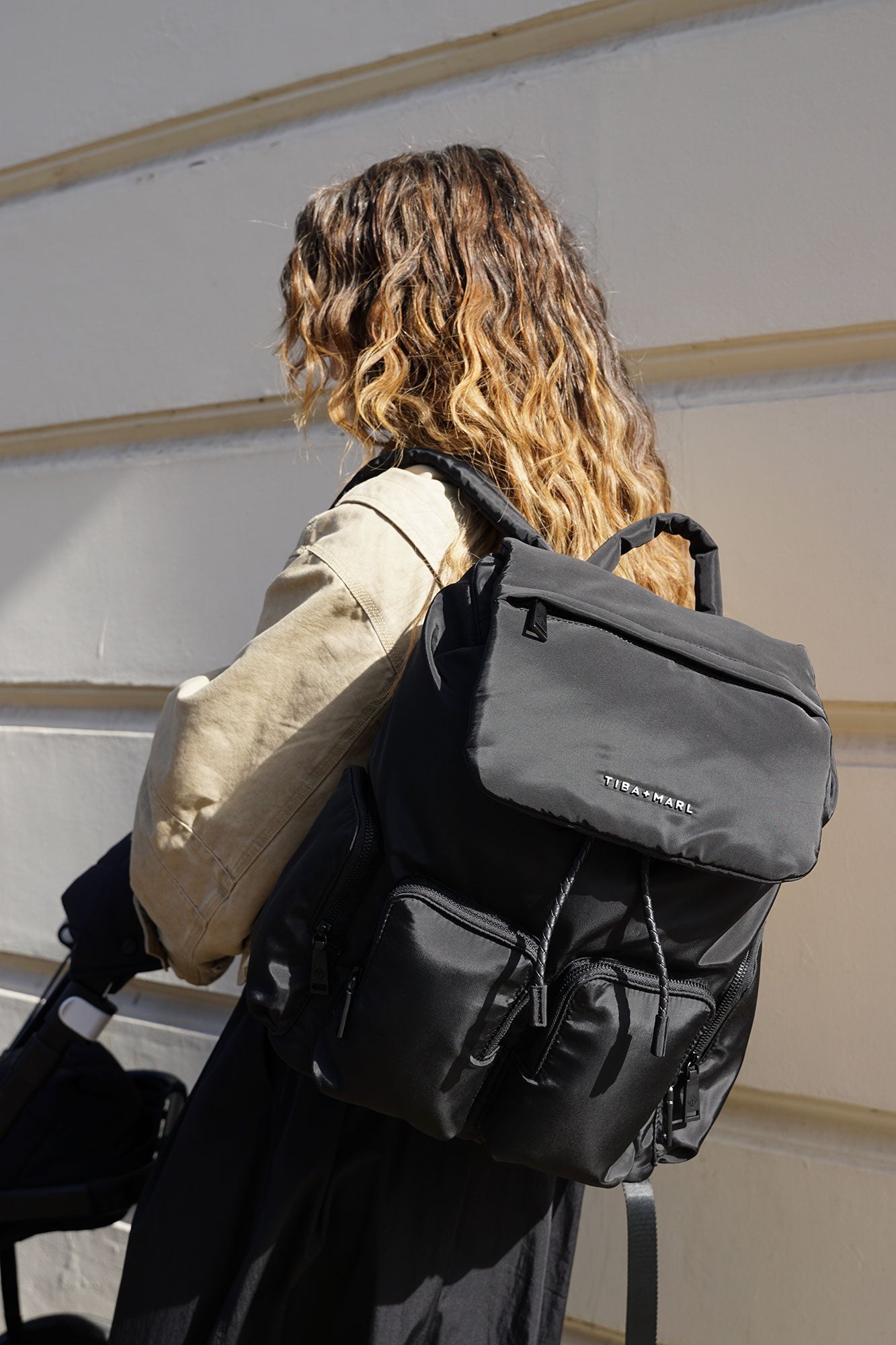 Person wearing a black backpack with visible branding against a neutral background pushing a buggy.