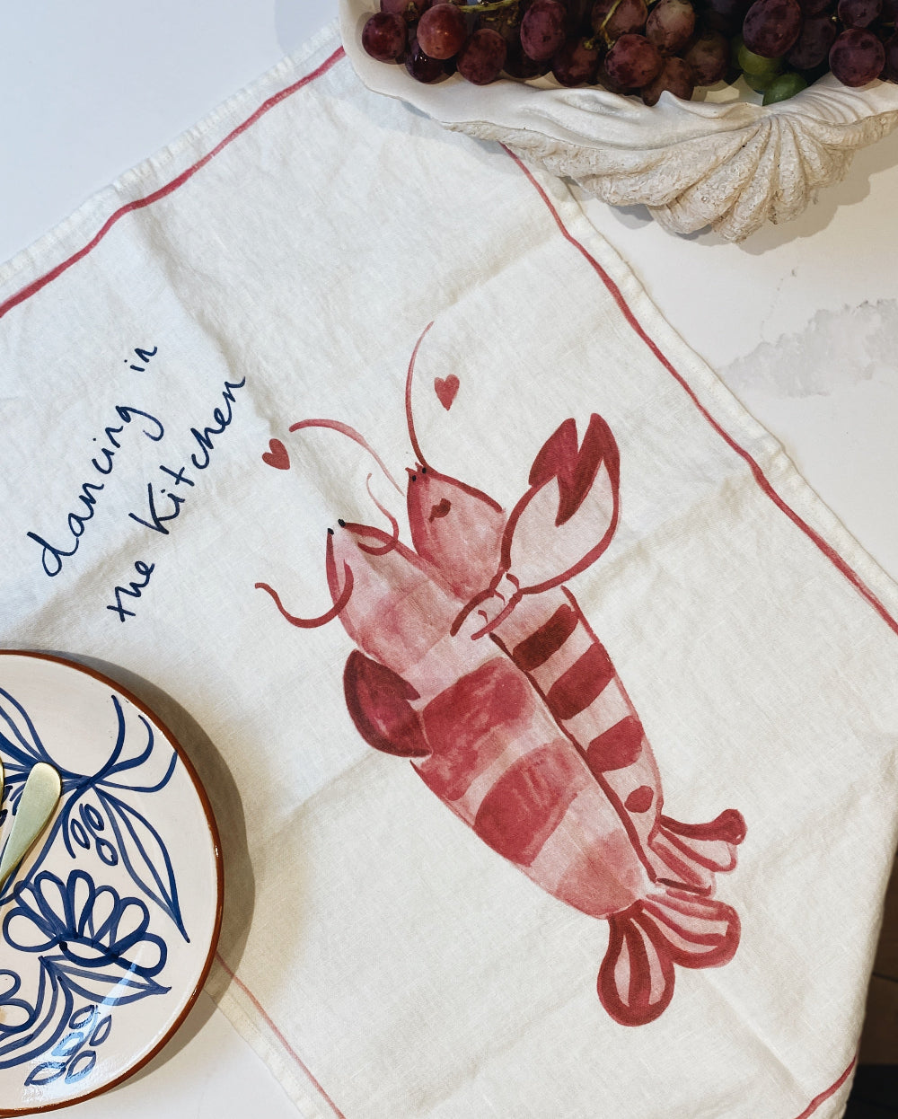 Tea towel with a red lobster design and text on a table setting.