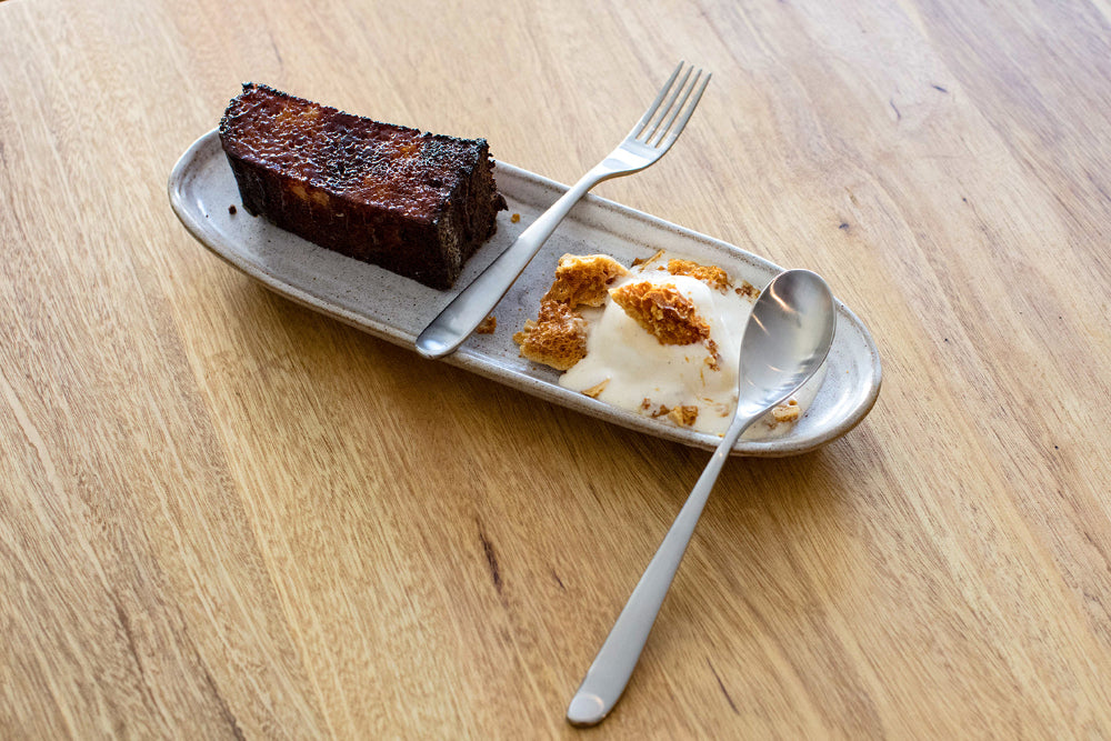 Slice of cake and ice cream on a plate with utensils on a wooden table.