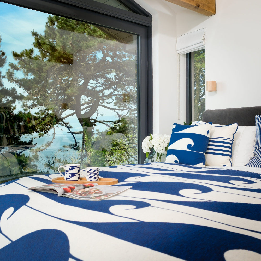 Bedroom with blue and white bedding, pillows, and a view of trees outside.