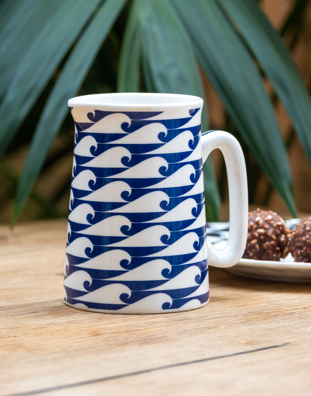 Mug with blue and white wave pattern on a wooden table with a blurred plant background