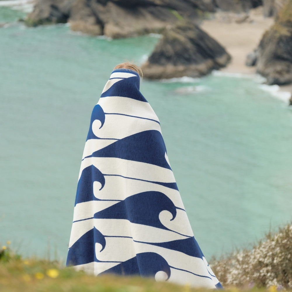Person wrapped in a blue and white patterned towel by a coastal landscape