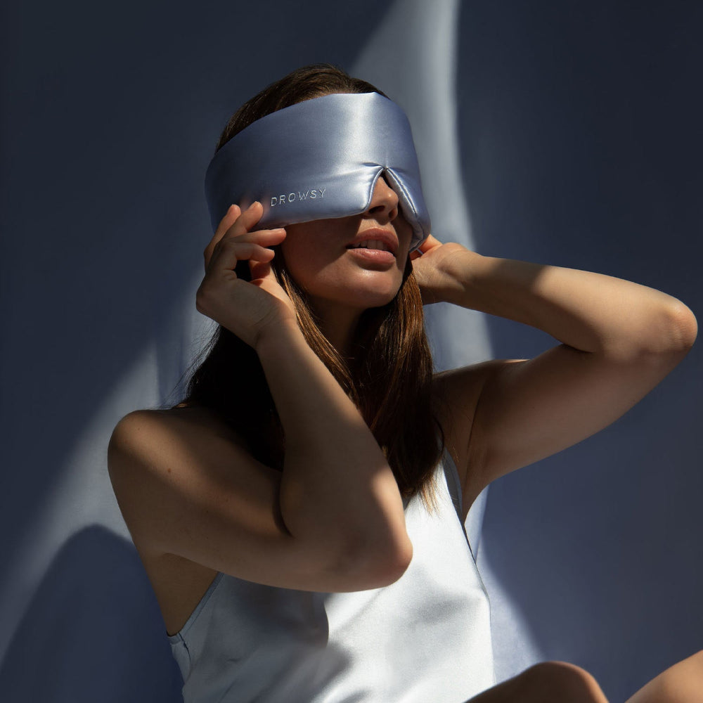 Person wearing a Drowsy Blue Belle silk sleep mask against a silk background