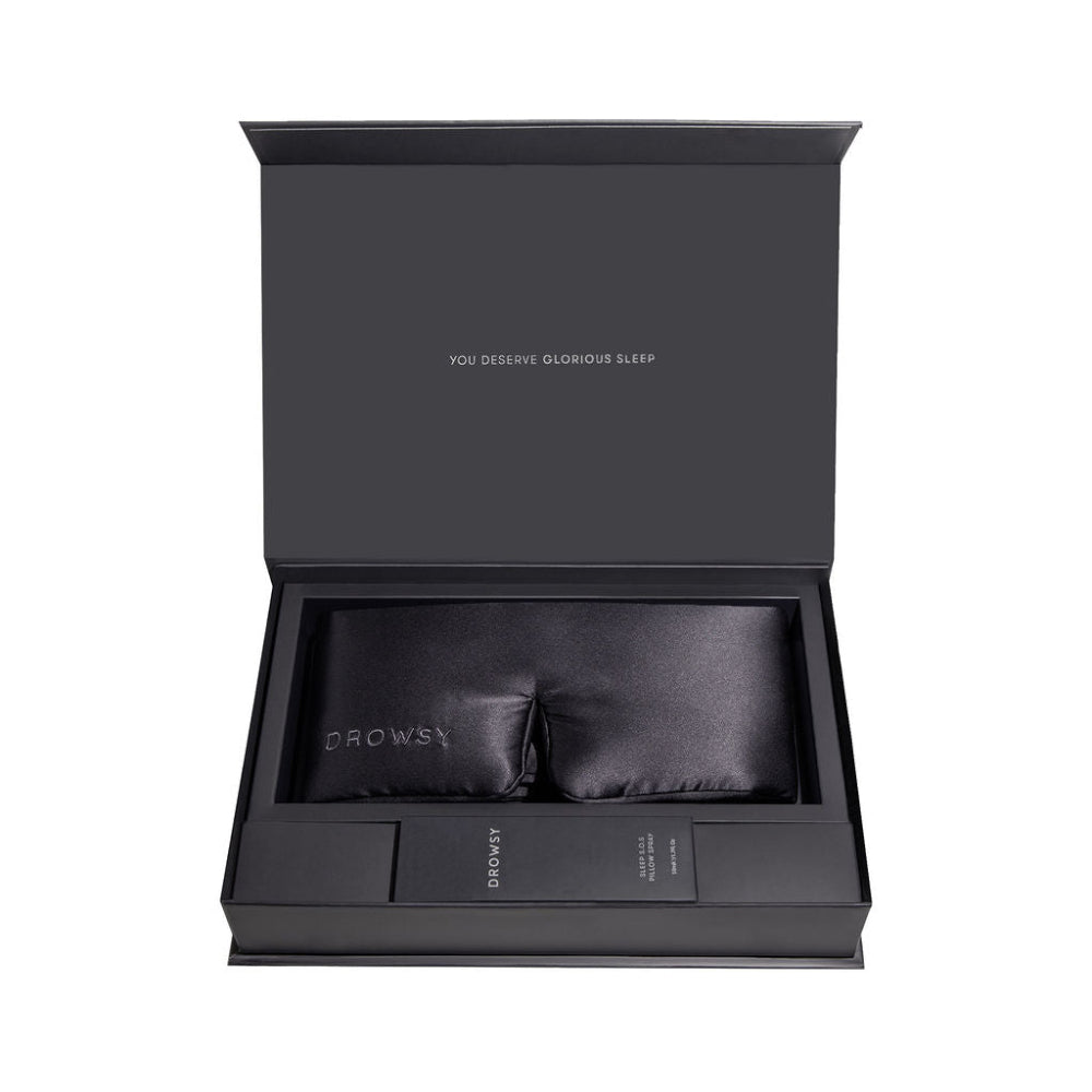 Black gift box with a silk black eye mask inside and sleep pillow spray on a white background