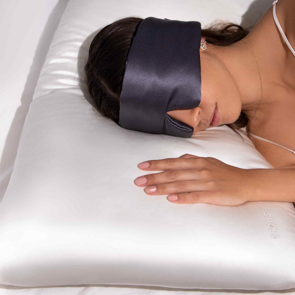 A woman laying on a White Silk pillowcase  with dark grey silk sleepmask