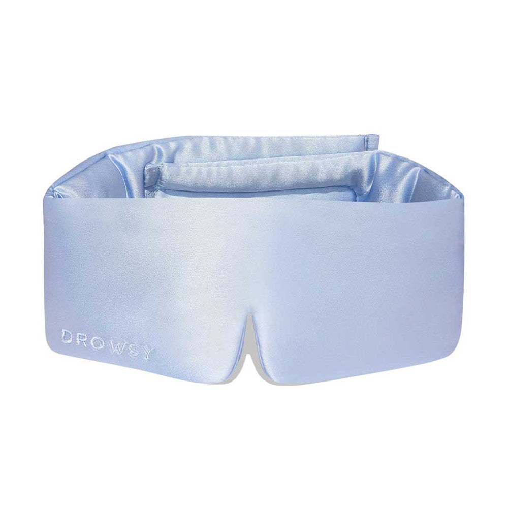 A baby blue silk sleep eye mask with a soft, padded design and the brand 'DROWSY' visible on the fabric.