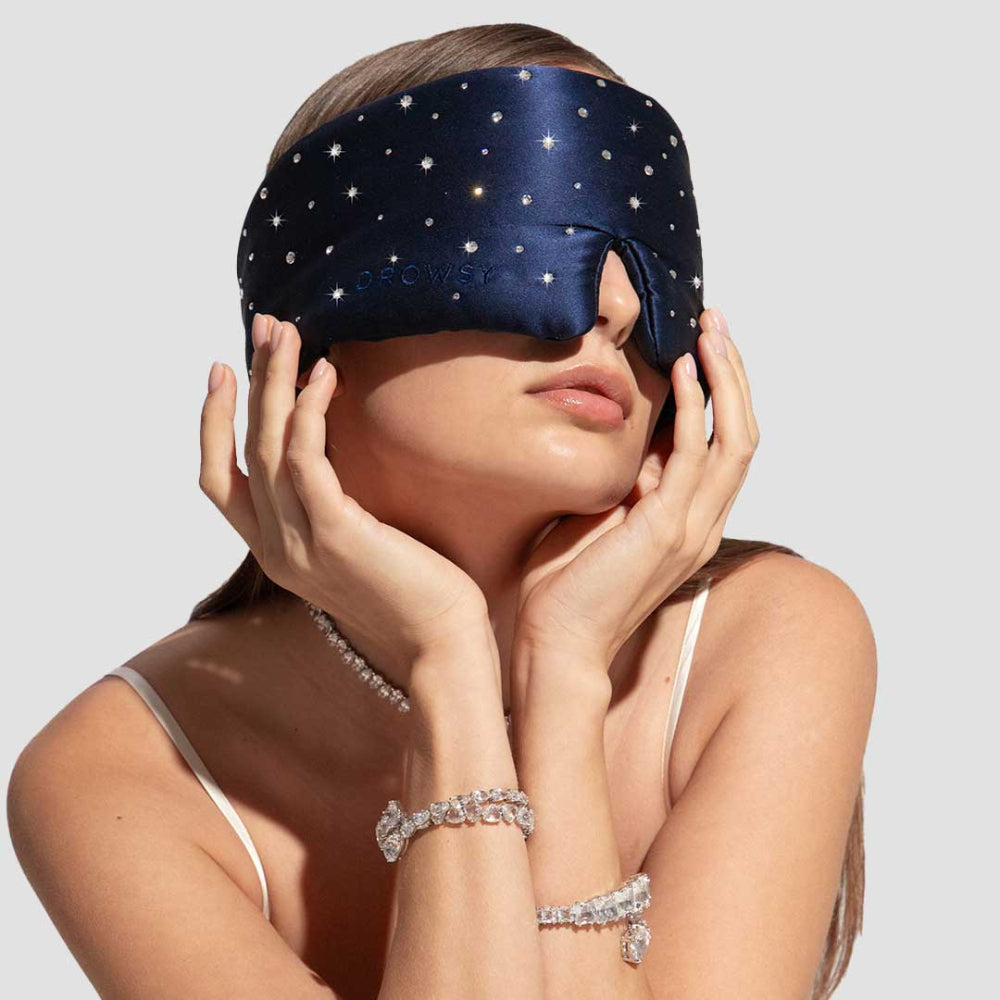 A person wearing a blue silk sleep mask embellished with crystals from Swarovski.