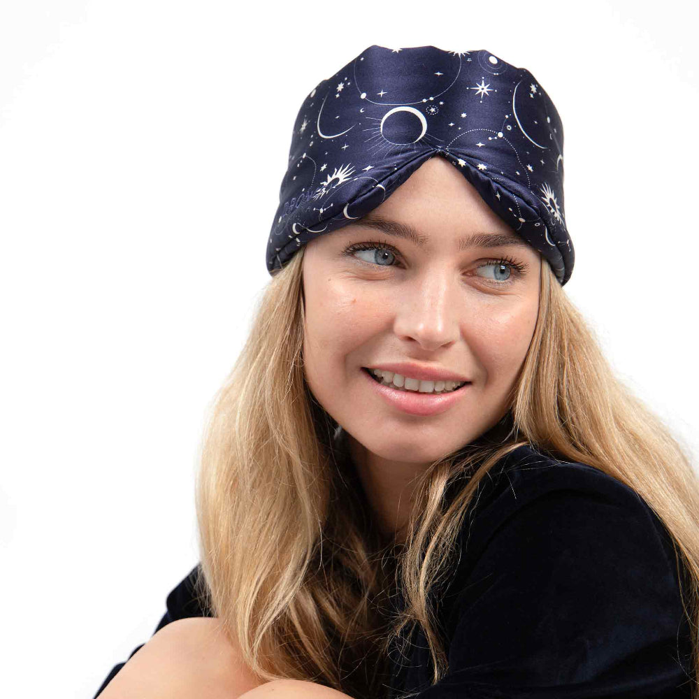 Woman wearing a Cosmic Energy blue eye mask with celestial pattern on a white background