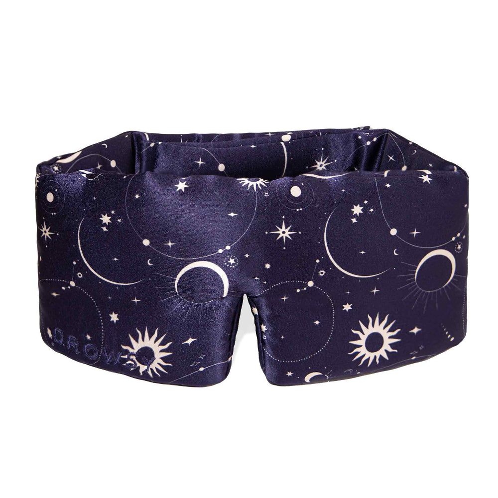 A deep blue Cosmic Energy silk sleep mask with a cosmic pattern featuring stars, moons, and suns.
