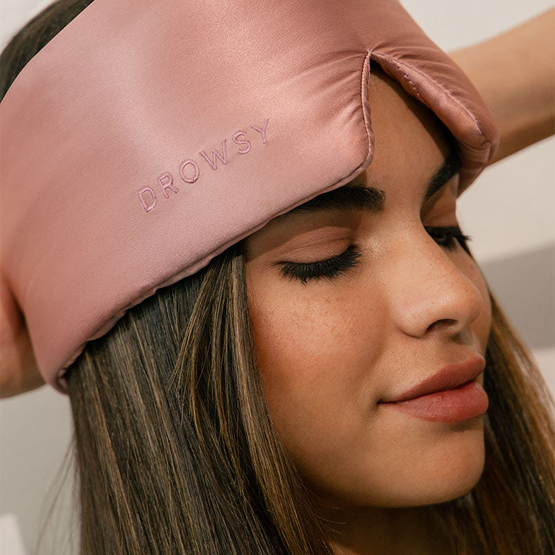 Person wearing a pink sleep eyelash cocoon mask with 'DROWSY' text.