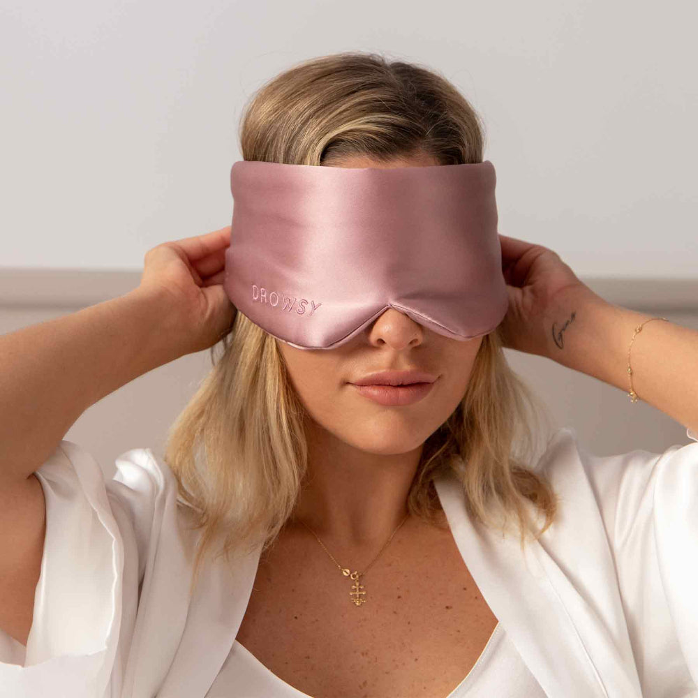 Woman wearing a Damask Rose pink silk sleep mask with a white dressing gown.