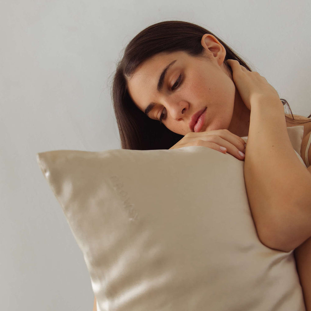 Woman sleeping with a Dusty Gold pillow against a plain background