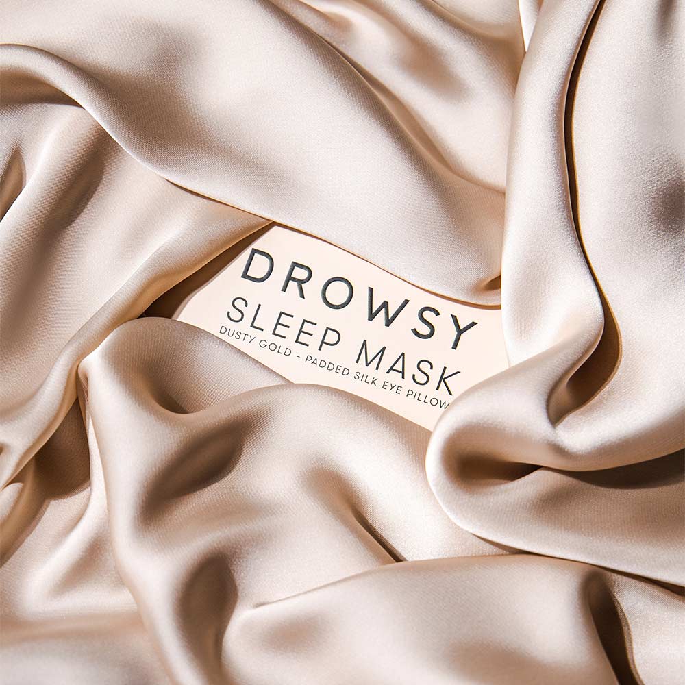 Silk Dusty Gold eye mask packaging with label 'Drowsy Sleep Mask' on a draped fabric background.