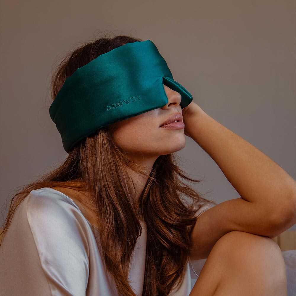 Person wearing a teal sleep mask with a neutral background.