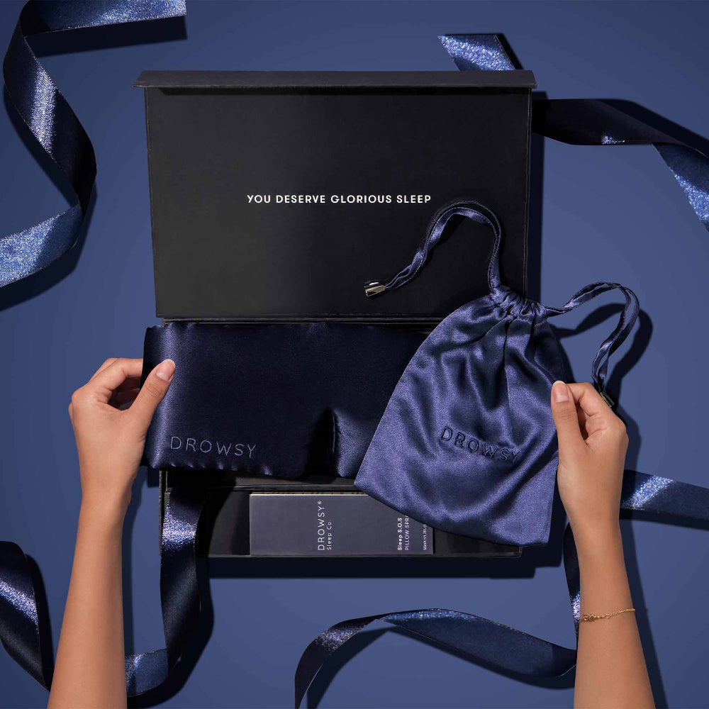 Silk sleep mask and packaging on a blue background with hands holding the items.