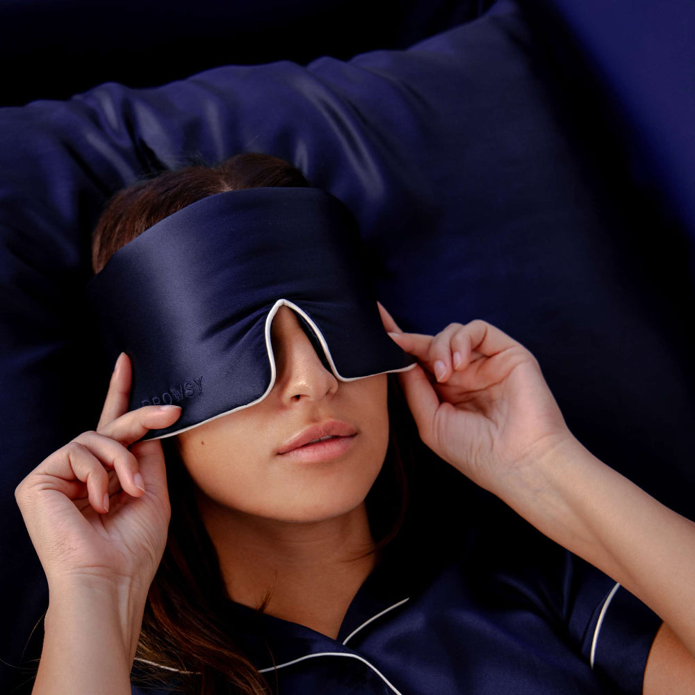 Model laying down wearing a midnight blue sleep mask on a midnight blue silk pillowcase