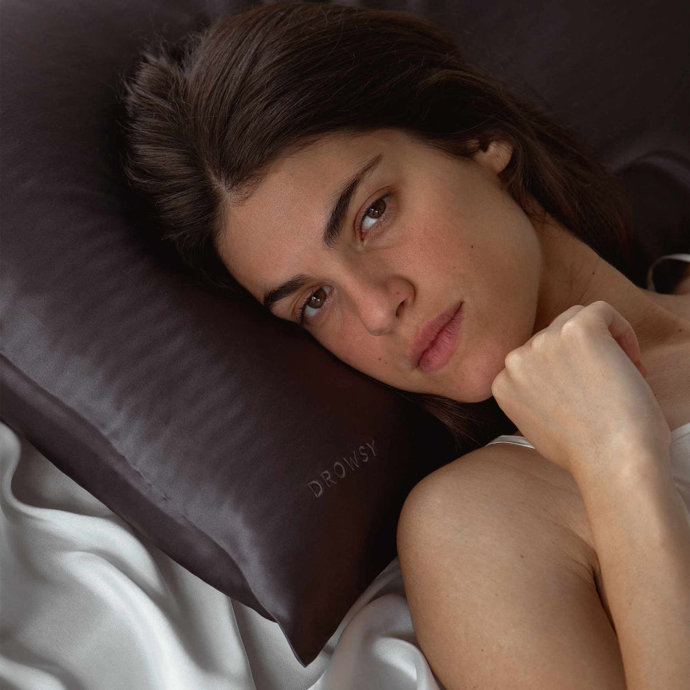 Woman with brown hair laying her head on a moonlight shadow coloured silk pillowcase 