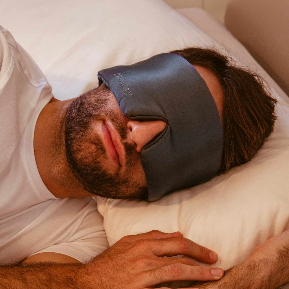 Man sleeping with a grey Mulberry silk sleep mask on his eyes laying on a pillow in bed.