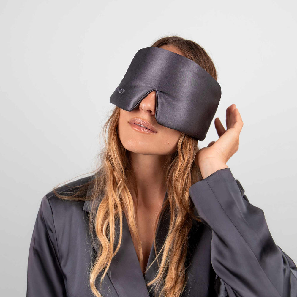 Person with long hair wearing a dark grey silk sleep mask