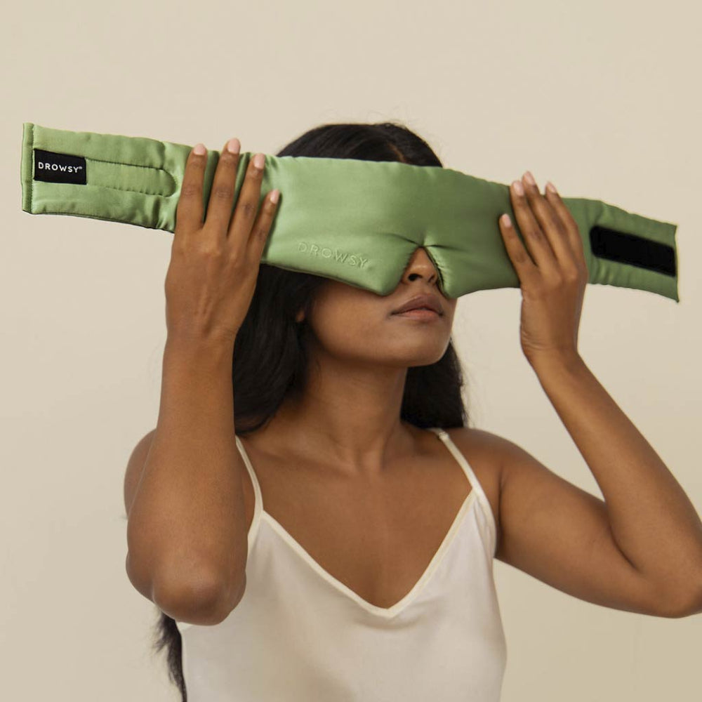 Person using a green sleep mask against a plain background