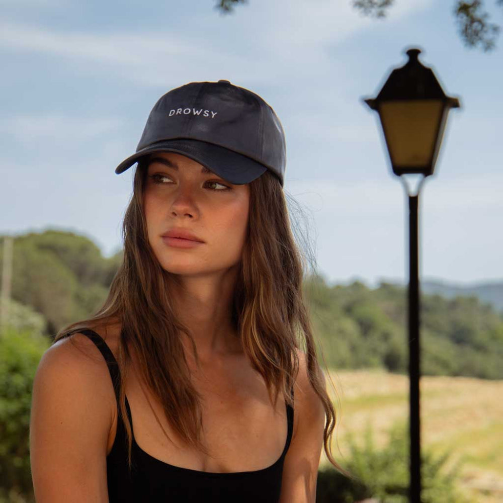 Woman wearing a black cap with 'Drowsy' logo outdoors