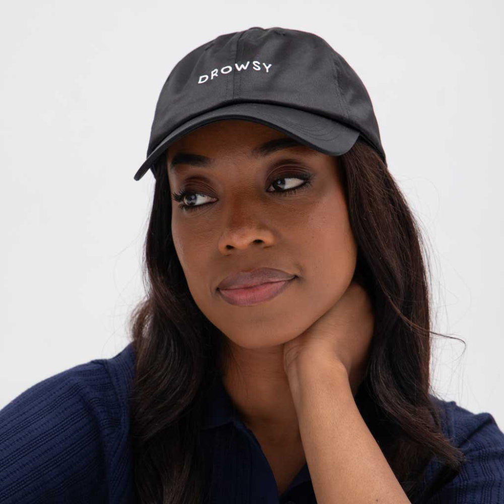 Woman wearing a black cap with 'DROWSY' text on a white background