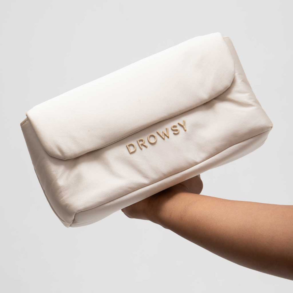 Dusty Gold makeup bag with 'Drowsy' branding held by a hand on a light grey background