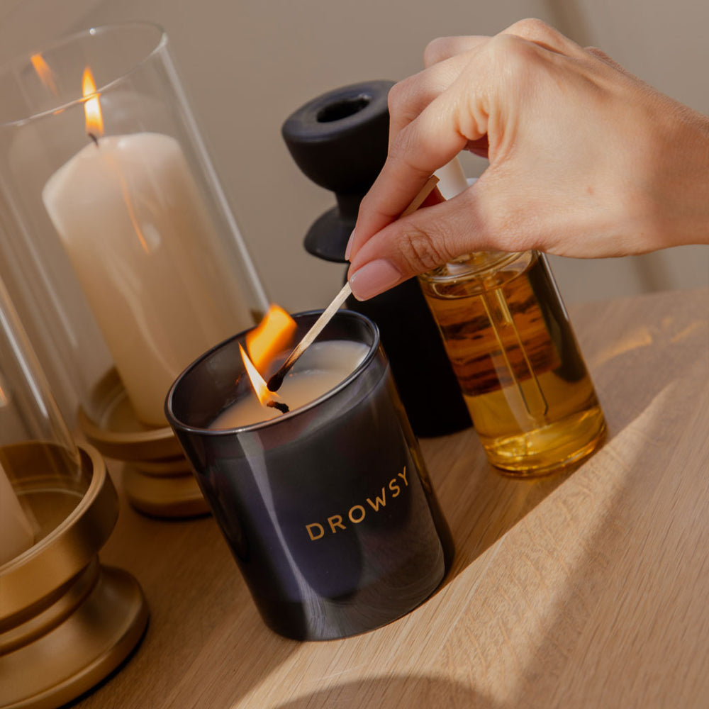 Person lighting a candle labeled 'Drowsy' with another candle in the background.