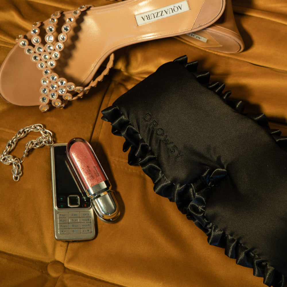 Shoe, phone, lip gloss, and black sleep mask on a brown fabric sofa