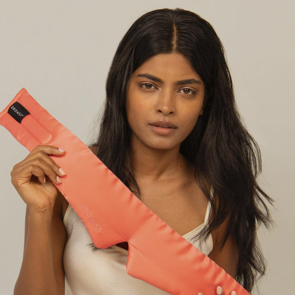 Woman holding a pink silk sleep mask against a plain background