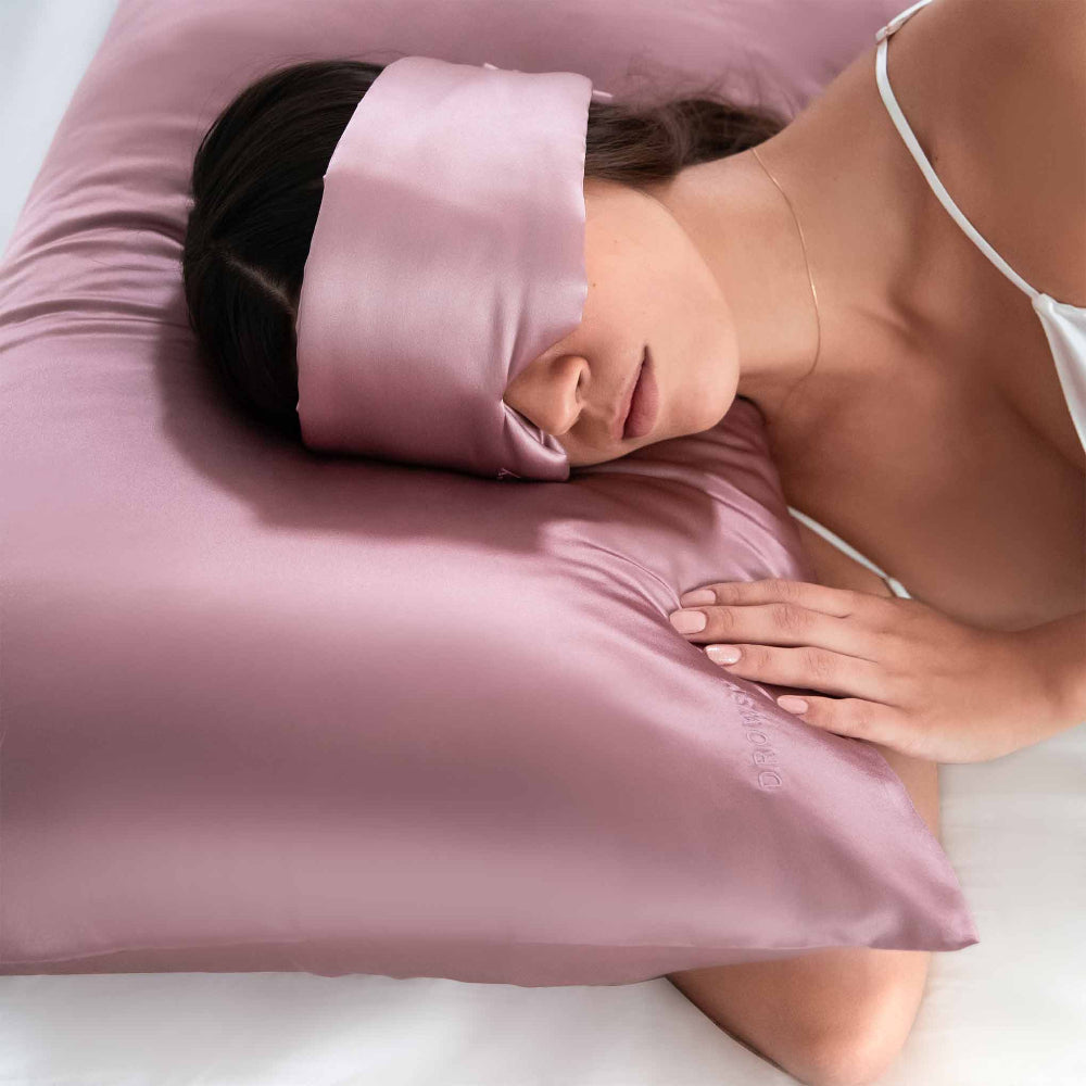 Person sleeping with a pink silk sleep mask laying on a matching pink coloured pillowcase