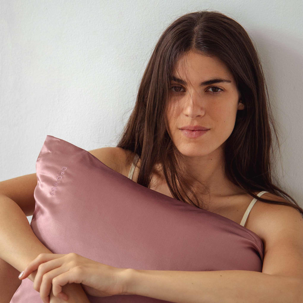 Woman holding a Damask pink silk pillowcase against a white background