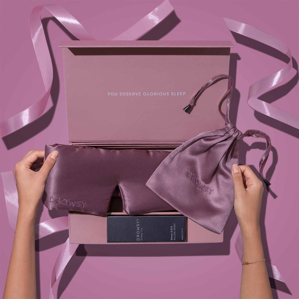 Silk sleep mask and pouch in a pink packaging box on a pink background.