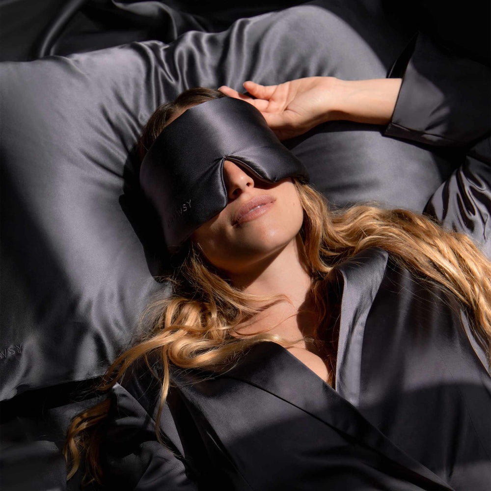 Woman laying on a bed wearing the moonlight shadow silk sleep mask on a moonligh shadow silk pillowcase