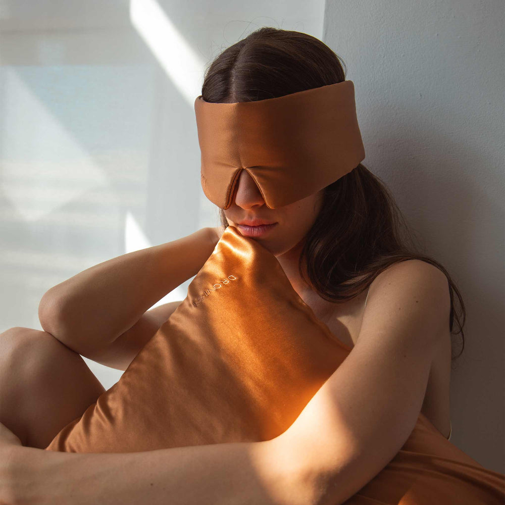 Woman wearing over her eyes the Drowsy Pumpkin Spice Tuscan Kiss Silk sleep mask holding matching silk pillow