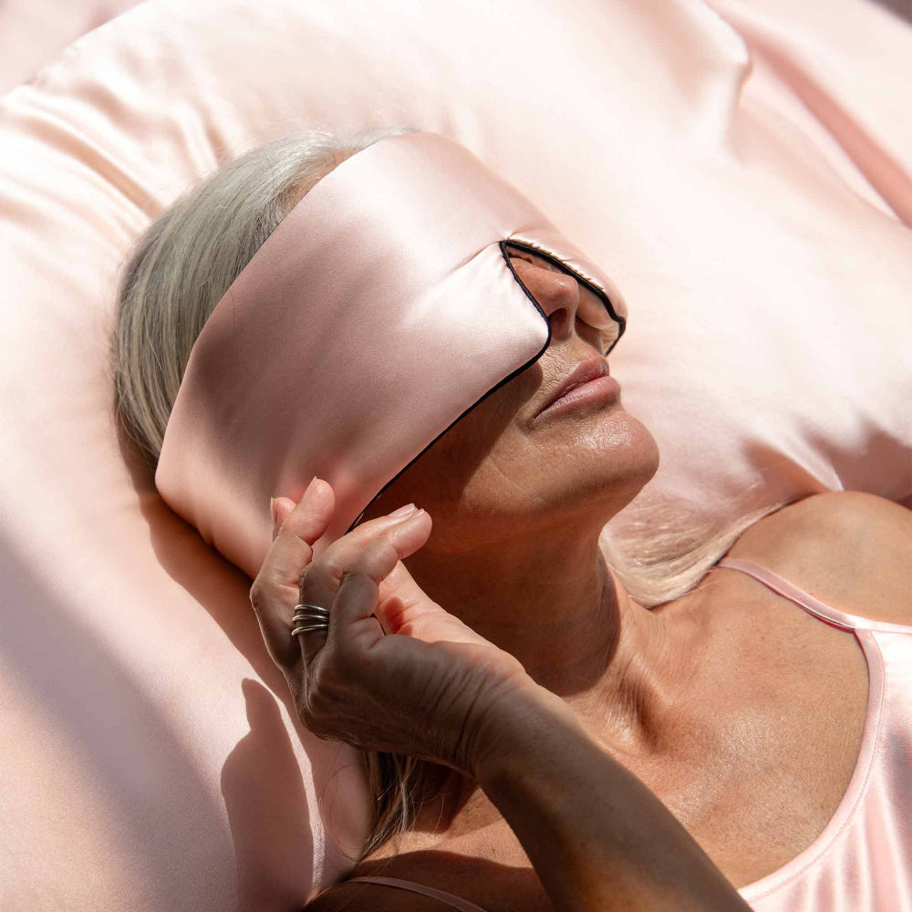 Person laying on a pink silk pillowcase with a pink sleep mask on.