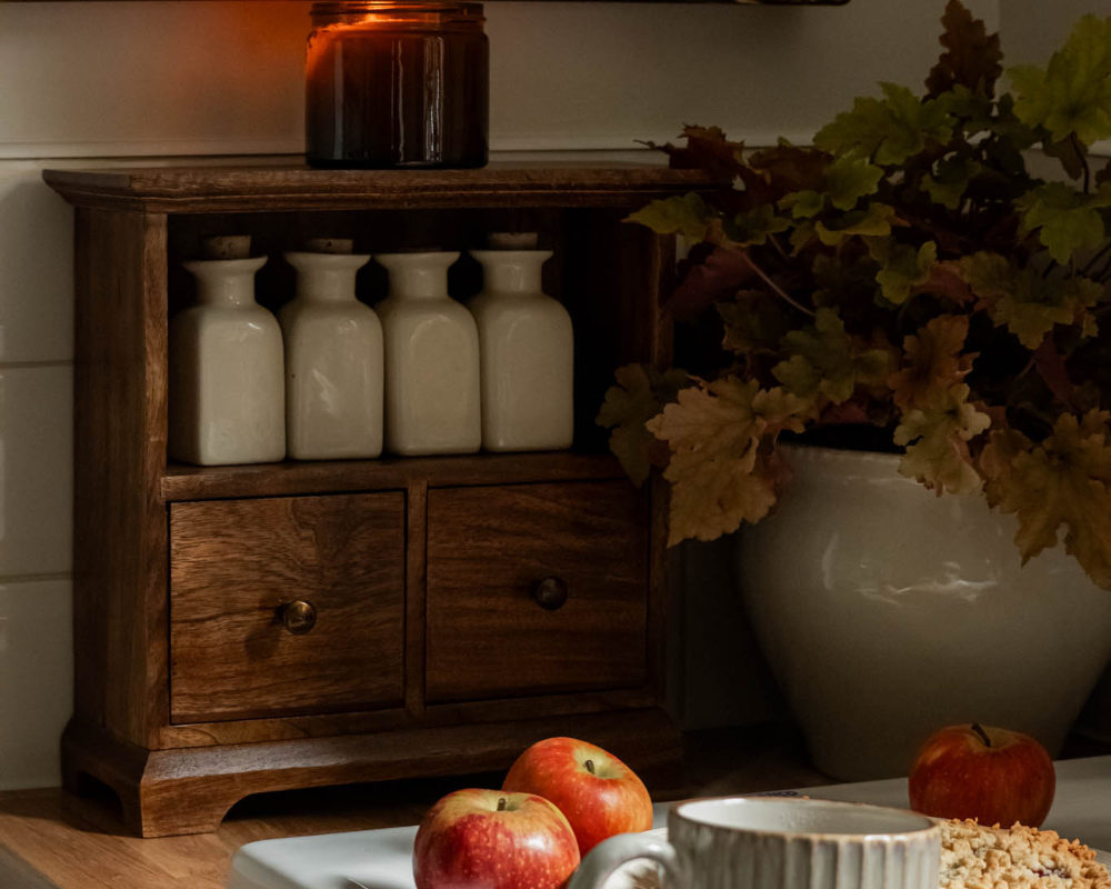 Wooden cabinet with white bottles, apples, and a vase on a table.