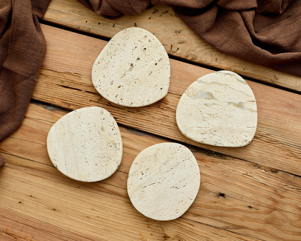Four irregular shaped stone coasters on a wooden surface with a brown fabric background