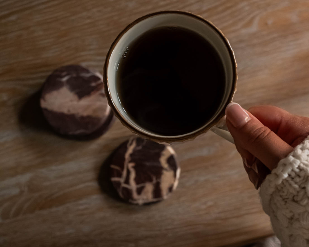 Hand holding a mug of hot chocolate on a wooden surface with decorative stones.