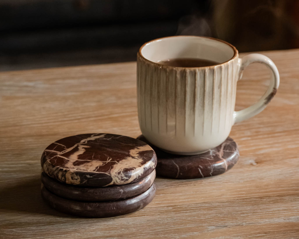 Ceramic mug with a textured design on a wooden surface, accompanied by three marble-patterned coasters.