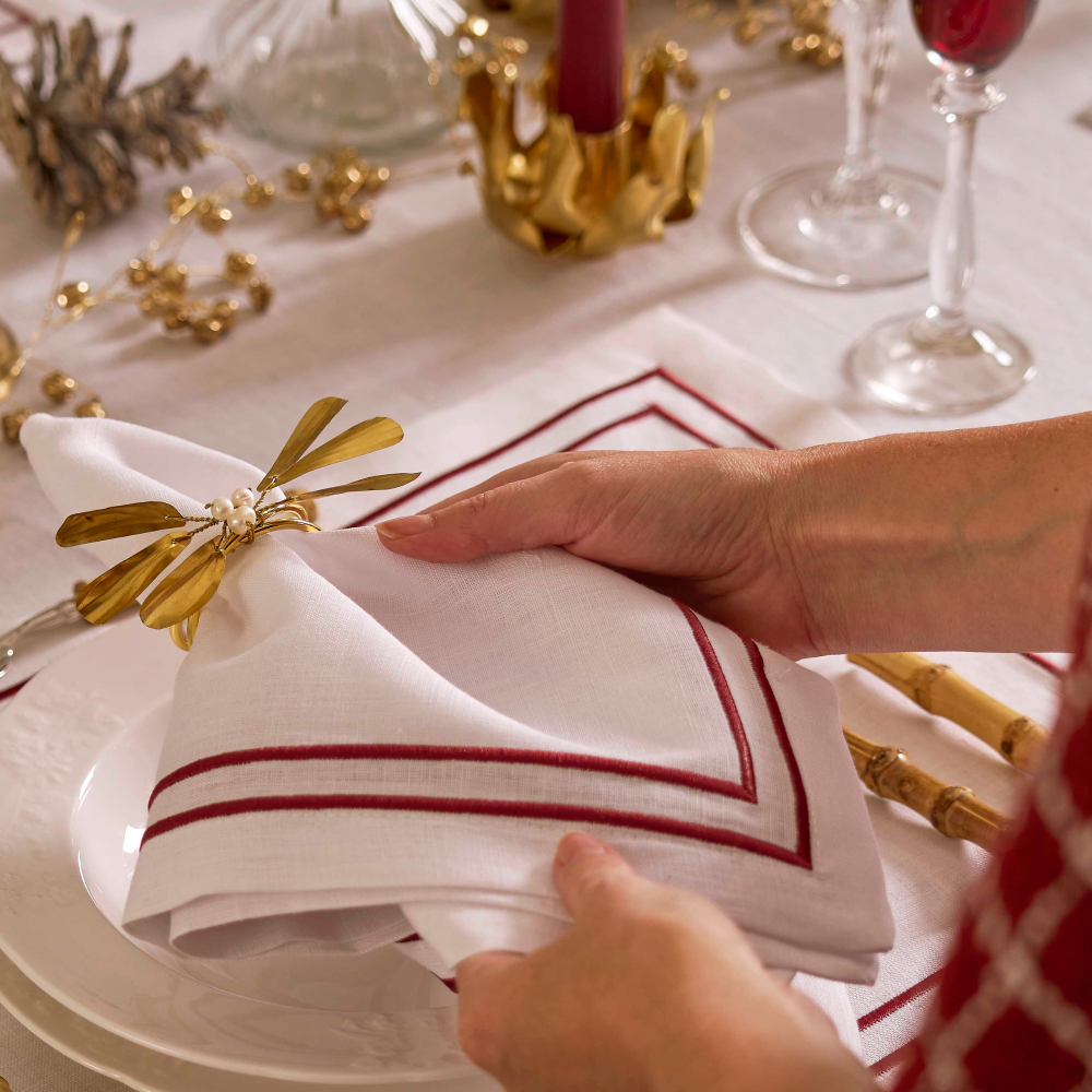 Person folding a white napkin with red stripes on a festive table setting.
