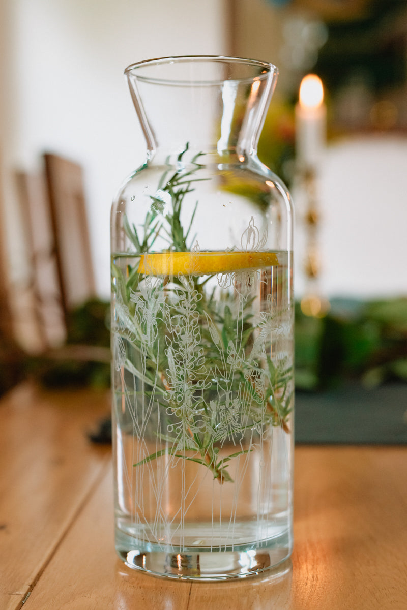 Clear glass Carafe with herbs in water on a wooden table