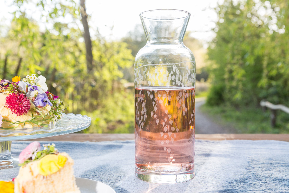 Clear glass carafe with floral arrangement and cake on a table outdoors