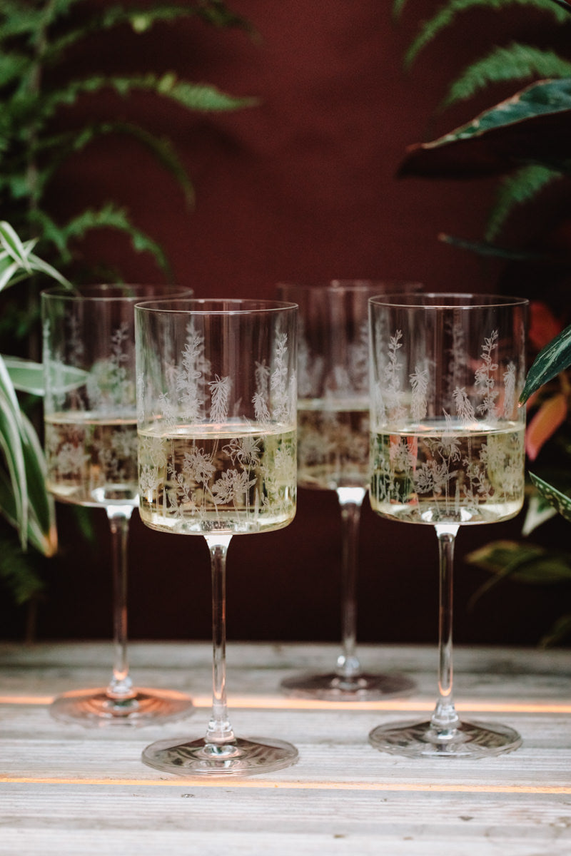 Four wine glasses with etched designs on a wooden surface with a blurred natural background