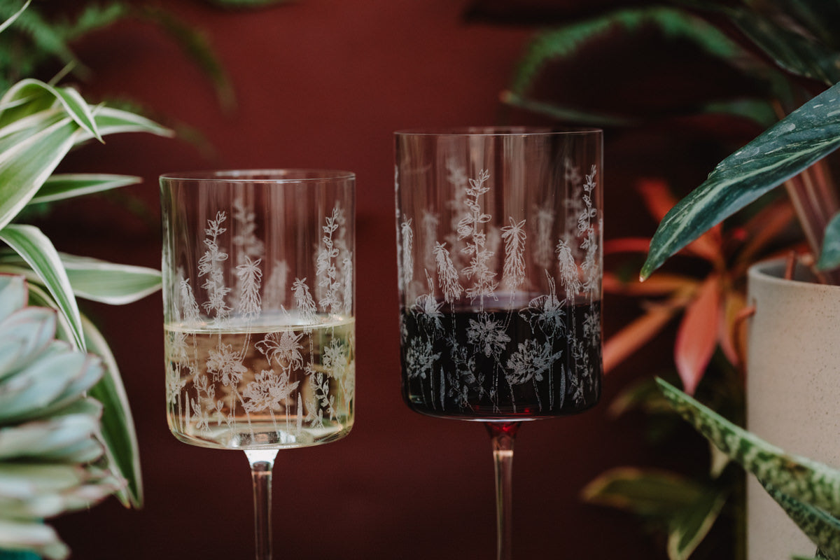 Two etched wine glasses with plants in the background